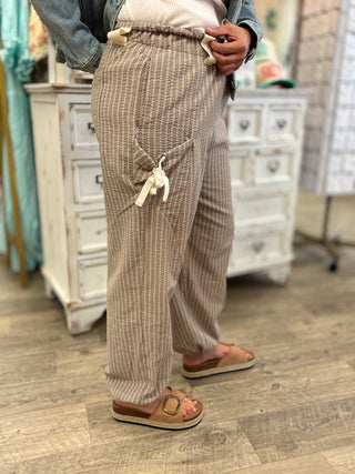 Model wearing taupe and cream striped pants with tie details