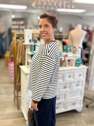 A woman modeling a cream and navy blue striped long-sleeve top and navy blue pants inside a boutique store.