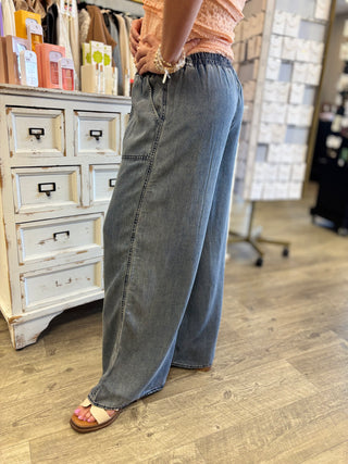 Person wearing blue jeans standing in a store with a wooden floor and white drawers in the background.