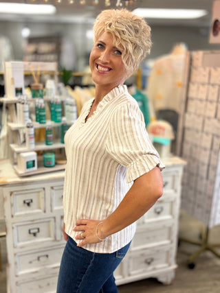 Model wearing cream and taupe striped top with ruffle detail