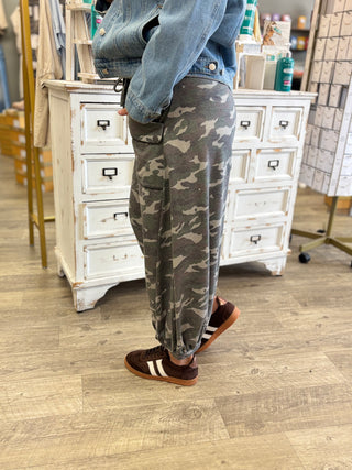 Model wearing loose fitting camo print jogger style pants with brown sneakers