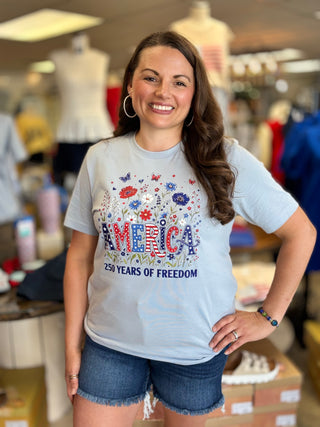 Woman wearing a t-shirt with 'America 250 Years of Freedom' design in a store setting.