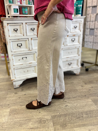 A person wearing a light beige wide-leg jeans with embroidery at the hem, paired with a pink top and brown flats, standing in a retail store.