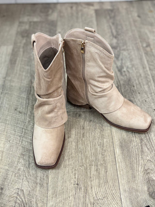A pair of beige suede hooded ankle boots with square toes and side zippers, displayed on a gray wood-look floor.