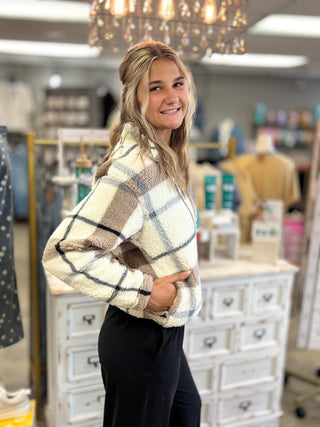 Model wearing a cream colored half zip top fleece top with taupe black and grey plaid detailing 
