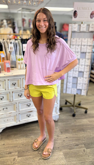 Model wearing a purple oversized shirt and yellow shorts in a store setting