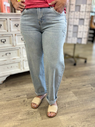 Model wearing light wash barrel denim jeans with flower patch detail