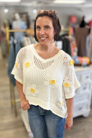 Woman wearing a white crochet top with yellow flowers in a store setting
