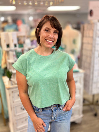 Woman wearing a green t-shirt and blue jeans standing in a store.