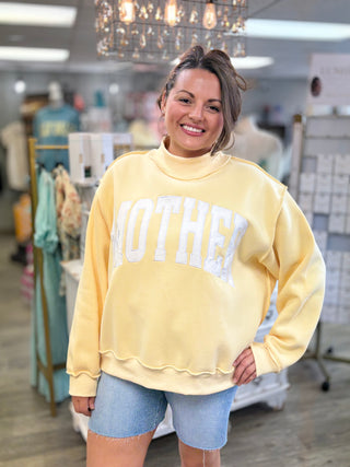 Model wearing butter yellow mock neck sweatshirt with ‘MOTHER’ embroidered on
