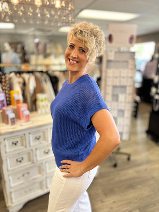 Side view of model wearing a cobalt blue sweater with white denim jeans