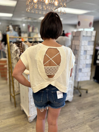 Model wearing cream color top with open back and denim shorts