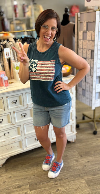 Woman wearing a sleeveless top with an American flag design and light wash denim shorts in a store setting
