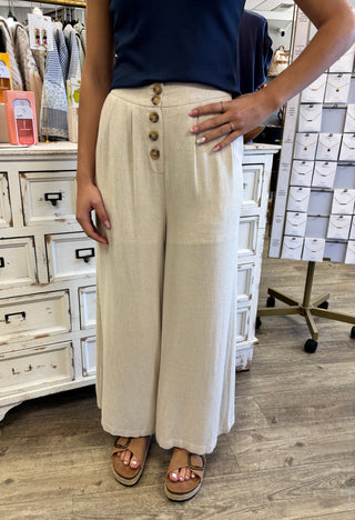 Person wearing beige wide-leg pants with buttons in a store setting
