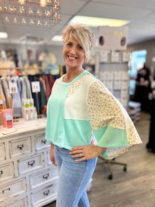 Woman wearing a light green and beige with floral pattern top in a store setting