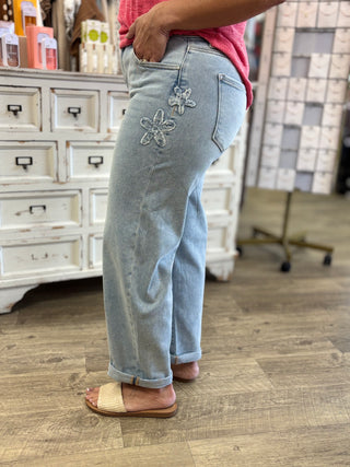 Model wearing light wash barrel denim jeans with flower patch detail