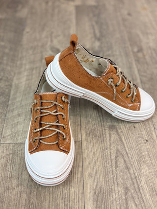 A pair of low-top platform sneakers in brown suede and canvas with chunky white soles, displayed on a gray wood-look floor.