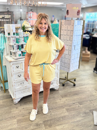 Woman in a yellow outfit standing in a store with various products and displays in the background.