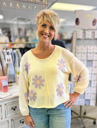 Woman wearing a cream sweater with lavender floral patterns in a store setting