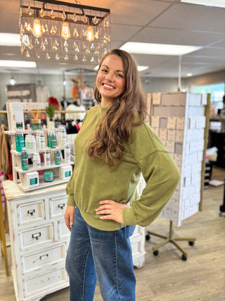 Model wearing a green mock neck long sleeve top with jeans