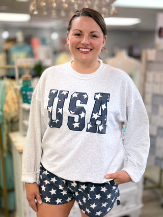 Woman wearing a light grey sweatshirt with 'USA' and star design, standing in a store.
