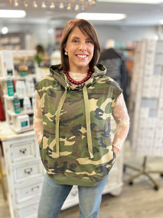 Model wearing a camo printed sleeveless top with a hood, lace long sleeve layer and denim