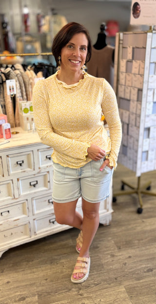 Model wearing yellow daisy print long sleeve top with denim shorts