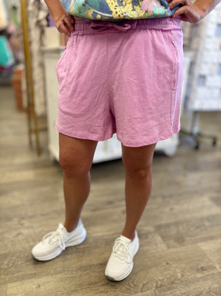 Model wearing pink shorts and white sneakers on a wooden floor.