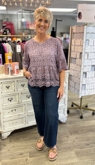 Woman wearing a purple patterned top and jeans standing in a store.