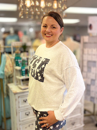 Woman wearing a light gray sweatshirt with ‘USA’ design in a store setting
