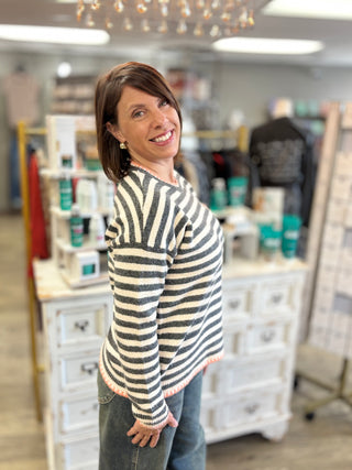 Model wearing a gunmetal grey and cream striped sweater with orange stitching detail and denim jeans