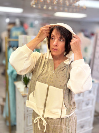 A woman wearing a beige and white patterned zip-up hoodie with white contrast panels and cuffs, standing in a boutique setting.