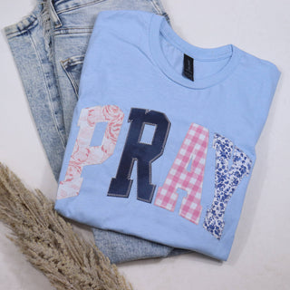 Light blue t-shirt with decorative letters 'PRAY' on a white surface with jeans.