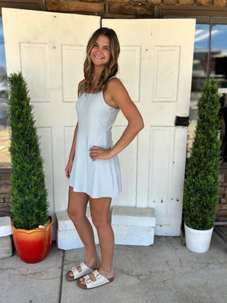 Woman in a light blue dress standing in front of a white door with two potted plants.