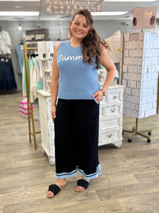Woman wearing a blue sleeveless top with 'Summer' text and black pants in a store setting.