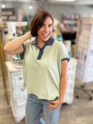 Model wearing an oversized top in sage green with blue trim and button detail