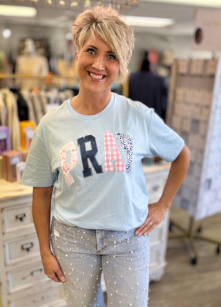 Woman wearing a light blue t-shirt with decorative letters spelling pray in a store setting