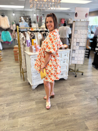 Model wearing orange and yellow floral dress in a store setting 