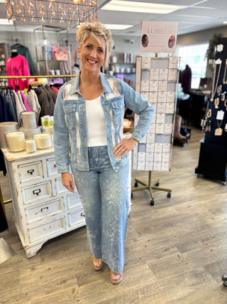 Woman in a denim outfit standing in a store with clothing racks and displays in the background.