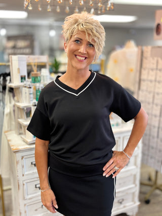 Model wearing black top with white piped trim