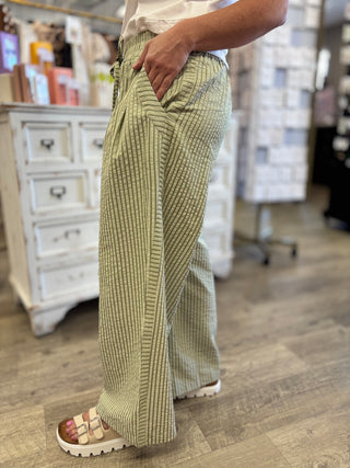 Model wearing two tones is olive green striped pants with elastic waist band and pockets