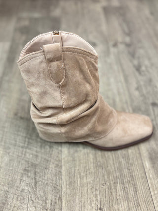 A single light beige suede western-style hooded boot with a low wedge heel, shown from a side profile on a gray wood-look floor.