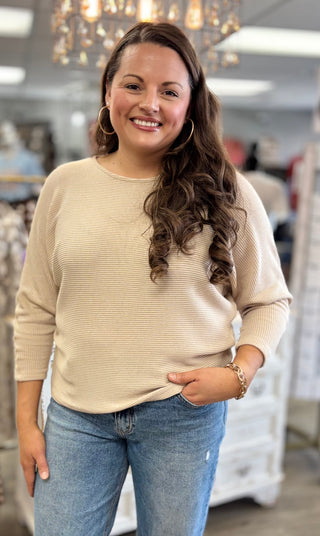 Woman wearing a beige sweater and blue jeans in a store setting