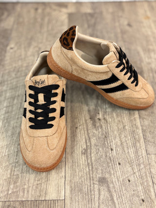 A pair of beige suede sneakers with black laces, black side stripes, a leopard print heel tab, and brown rubber soles, displayed on a gray wood plank floor.
