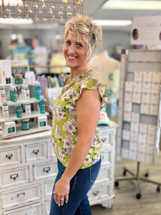 Woman in a green and purple floral top standing in a store setting.