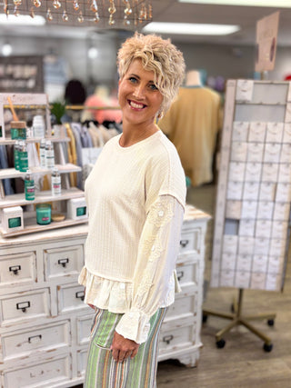 Model wearing a cream colored, multi-textured top with striped pants