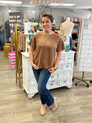 Woman wearing the Salted Caramel Suede Top, a camel faux suede short sleeve blouse with a round neckline and contrast stitching, styled with dark jeans and tan ankle boots