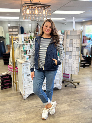 Model wearing a navy quilted vest with a navy and white striped long sleeve top and jeans.
