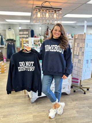 Model wearing navy mock neck sweatshirt with HOMEBOY graphic and holding the reverse of the sweatshirt with DO NOT DISTURB graphic