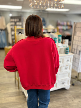 A person viewed from behind wearing a bright red oversized crewneck sweatshirt and blue jeans inside a retail store.